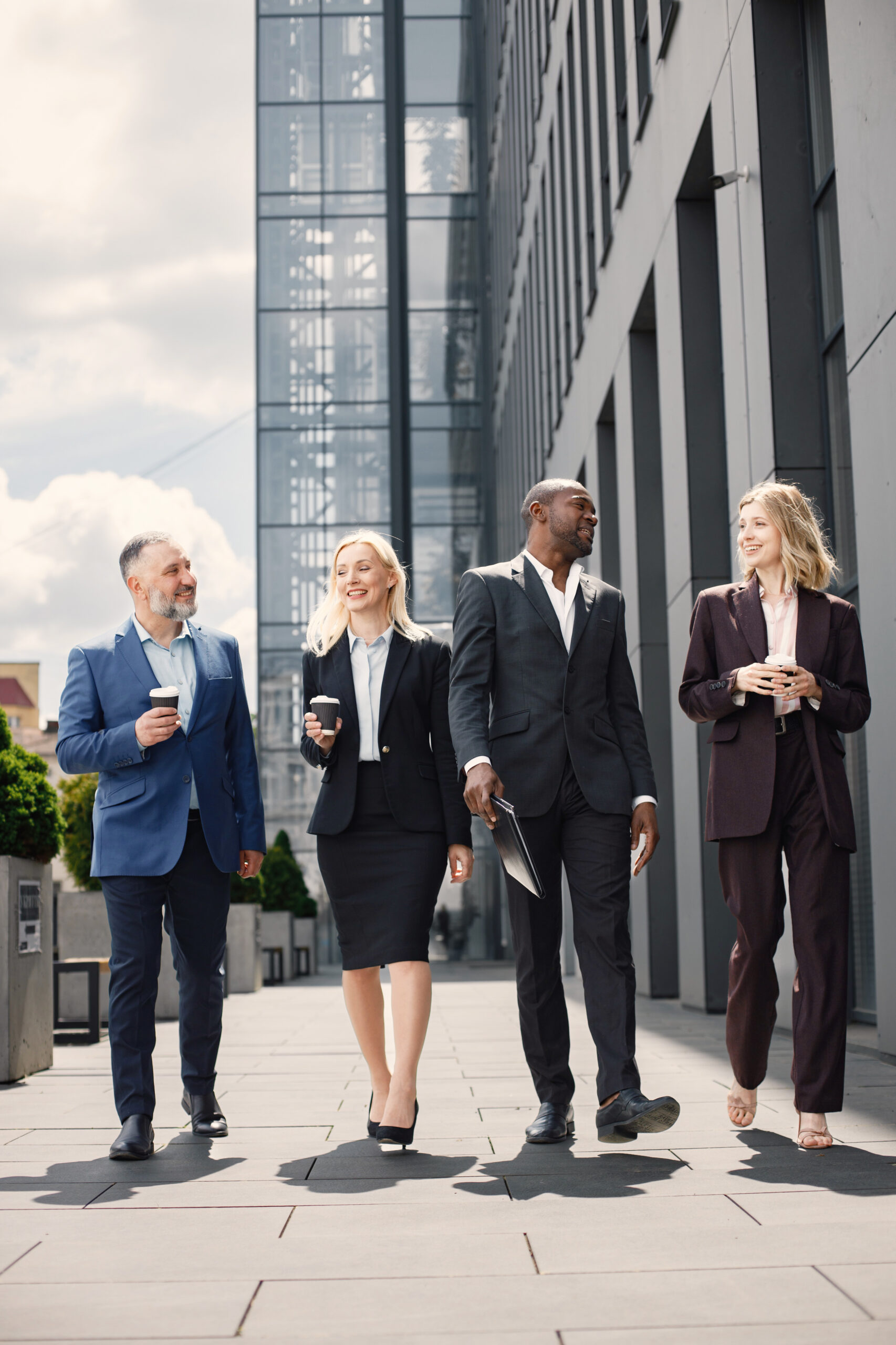 Business people standing and talk to each other in front of mode Confident businesspeople standing in front of modern office building. Men and women talking and looking at documents. Banking and financial market concept.